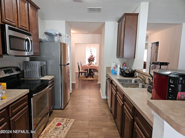 kitchen with stainless steel appliances, a textured ceiling, sink, and light wood-type flooring