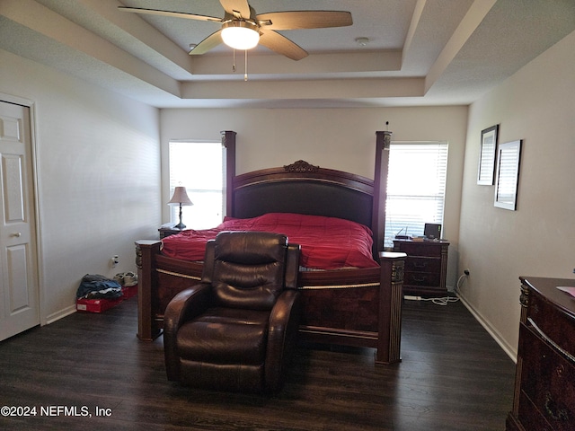 bedroom with a tray ceiling, dark wood-type flooring, and ceiling fan