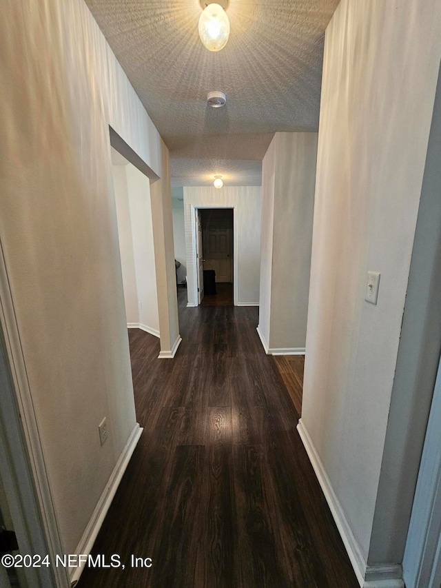 hall with a textured ceiling and dark hardwood / wood-style flooring