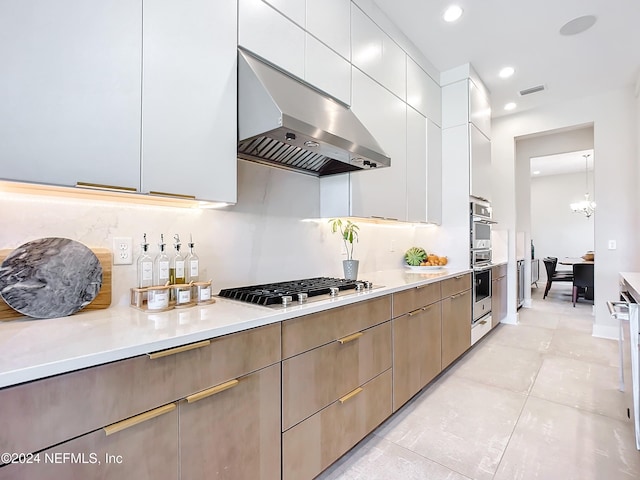 kitchen featuring appliances with stainless steel finishes, wall chimney range hood, decorative light fixtures, white cabinets, and light tile patterned flooring