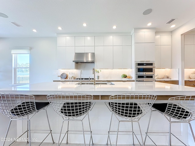 kitchen featuring double oven, a large island, white cabinets, and range hood