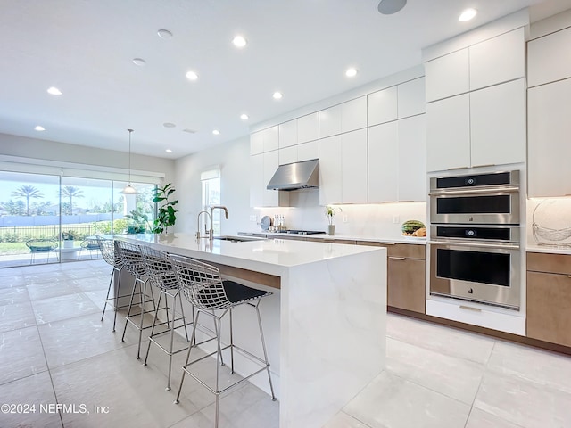 kitchen featuring appliances with stainless steel finishes, sink, exhaust hood, pendant lighting, and a center island with sink