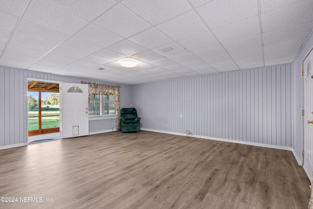 unfurnished living room featuring a paneled ceiling, hardwood / wood-style flooring, and wooden walls