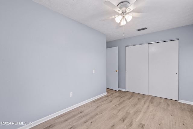 unfurnished bedroom featuring a textured ceiling, a closet, light hardwood / wood-style flooring, and ceiling fan