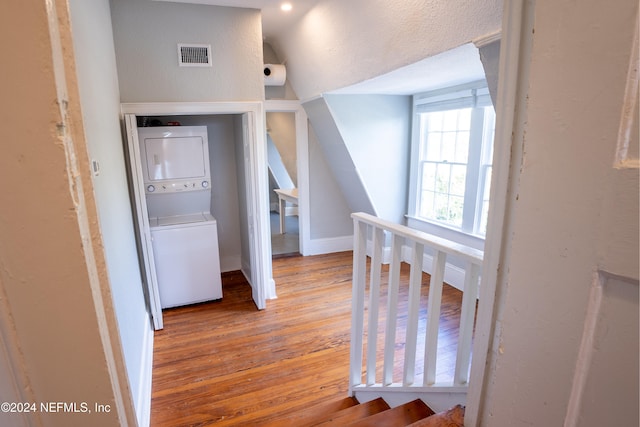 hall with stacked washing maching and dryer, light hardwood / wood-style floors, and lofted ceiling