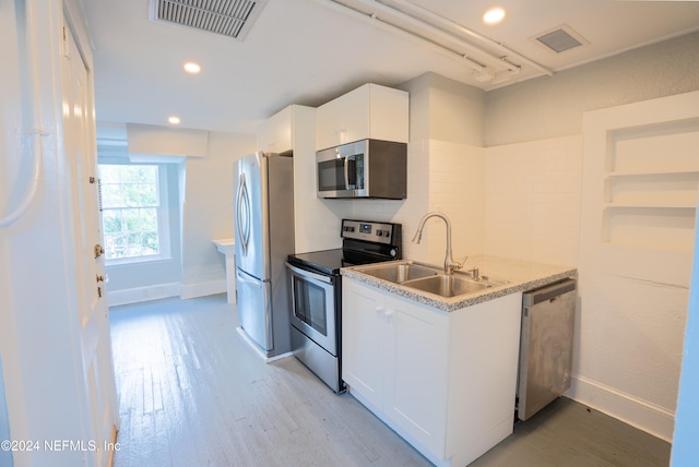 kitchen featuring light stone counters, light wood-type flooring, appliances with stainless steel finishes, sink, and white cabinets