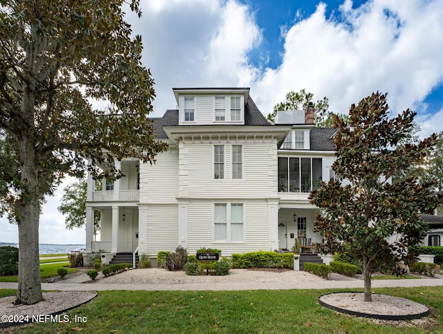 view of front facade featuring a water view, a front lawn, and a balcony