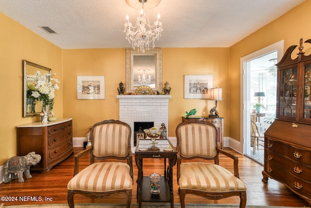 living area featuring an inviting chandelier, a textured ceiling, wood-type flooring, and a fireplace