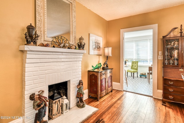 sitting room featuring hardwood / wood-style floors, a textured ceiling, and a brick fireplace