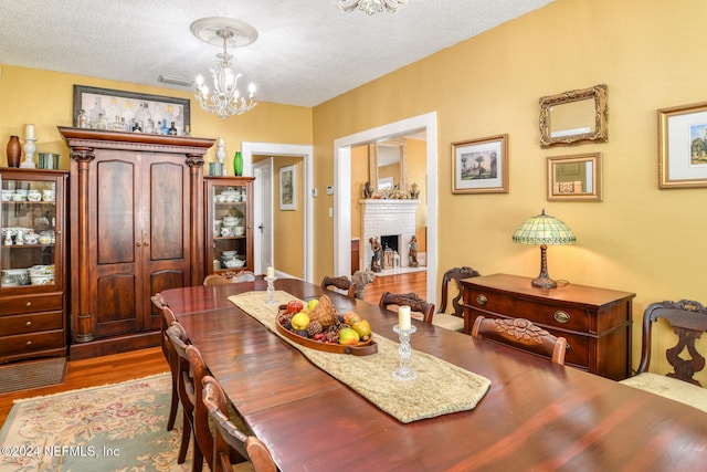 dining room with a notable chandelier, a fireplace, a textured ceiling, and light hardwood / wood-style floors