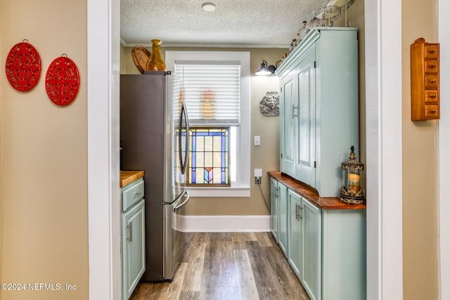 kitchen featuring butcher block counters, a textured ceiling, dark hardwood / wood-style flooring, stainless steel fridge, and crown molding