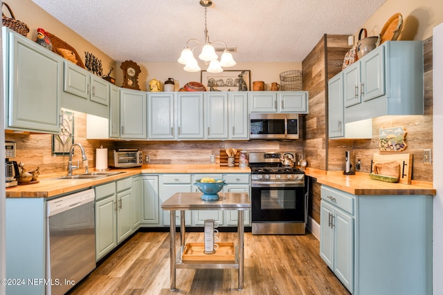 kitchen featuring appliances with stainless steel finishes, sink, decorative light fixtures, butcher block countertops, and a textured ceiling