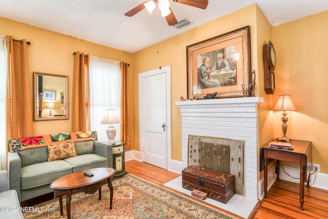 living room featuring light hardwood / wood-style flooring, a brick fireplace, a textured ceiling, and ceiling fan