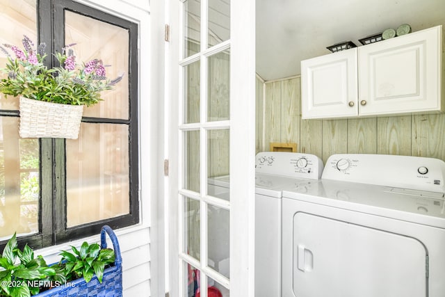 laundry area with cabinets, wooden walls, and washer and clothes dryer