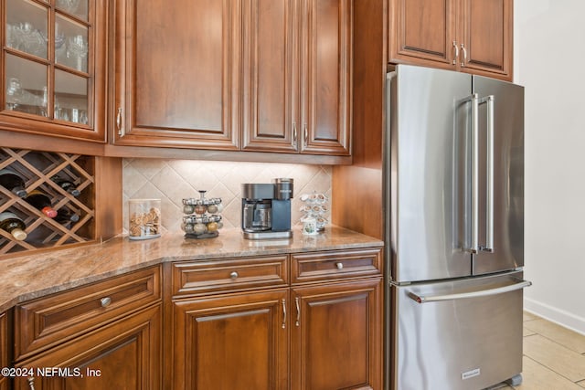 kitchen featuring light tile patterned flooring, high end refrigerator, light stone countertops, and decorative backsplash