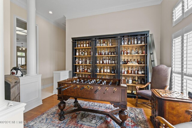 interior space featuring decorative columns, ornamental molding, ceiling fan, hardwood / wood-style floors, and bar area