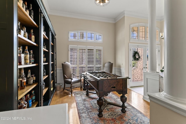 rec room with hardwood / wood-style flooring, ornamental molding, a towering ceiling, and decorative columns