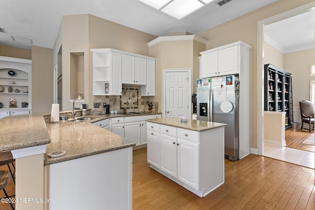 kitchen with stainless steel fridge, light wood-type flooring, kitchen peninsula, and white cabinetry