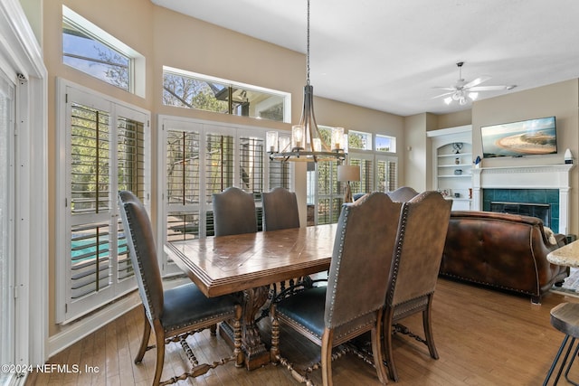 dining room featuring ceiling fan with notable chandelier, wood-type flooring, and a tiled fireplace