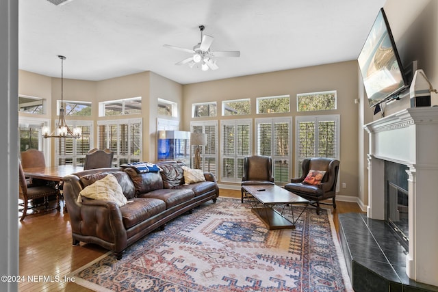 living room with a tile fireplace, dark wood-type flooring, and ceiling fan with notable chandelier