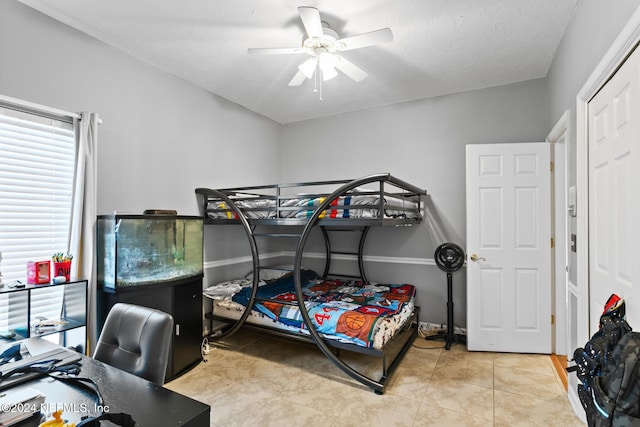 bedroom featuring ceiling fan, light tile patterned floors, and a textured ceiling