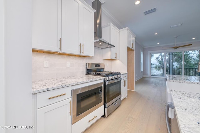 kitchen with white cabinetry, stainless steel appliances, wall chimney range hood, crown molding, and light wood-type flooring