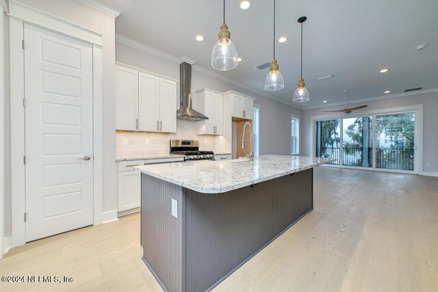 kitchen with ceiling fan, white cabinetry, wall chimney exhaust hood, a large island, and stainless steel gas range