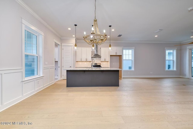 kitchen featuring light wood-type flooring, ornamental molding, pendant lighting, a center island with sink, and white cabinetry