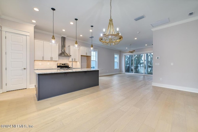 kitchen with wall chimney range hood, decorative light fixtures, white cabinets, light hardwood / wood-style floors, and a large island