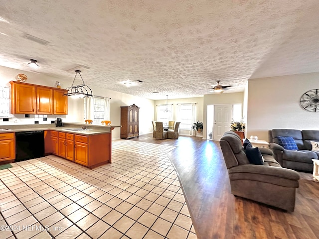 kitchen with kitchen peninsula, hanging light fixtures, a textured ceiling, dishwasher, and light hardwood / wood-style floors