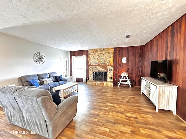 living room with hardwood / wood-style flooring, a textured ceiling, wooden walls, and a fireplace