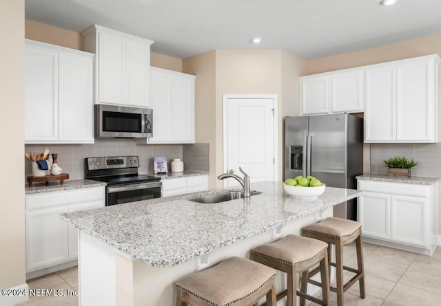 kitchen featuring stainless steel appliances, white cabinetry, sink, and a center island with sink