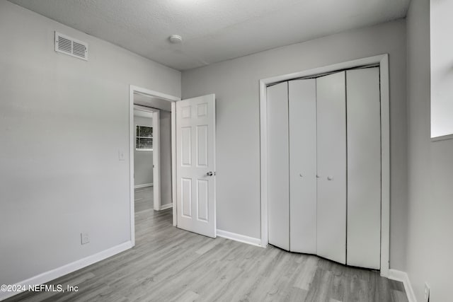 unfurnished bedroom featuring light hardwood / wood-style floors, a closet, a textured ceiling, and multiple windows