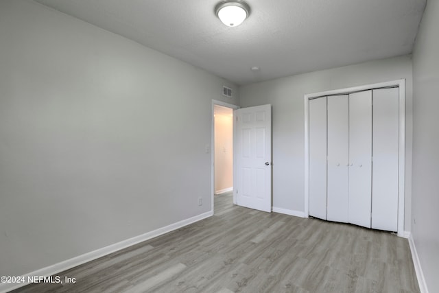 unfurnished bedroom featuring light hardwood / wood-style flooring, a textured ceiling, and a closet