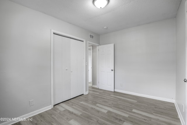 unfurnished bedroom featuring a closet, a textured ceiling, and light wood-type flooring