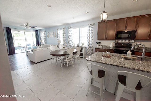 kitchen featuring light stone countertops, ceiling fan, sink, black appliances, and pendant lighting