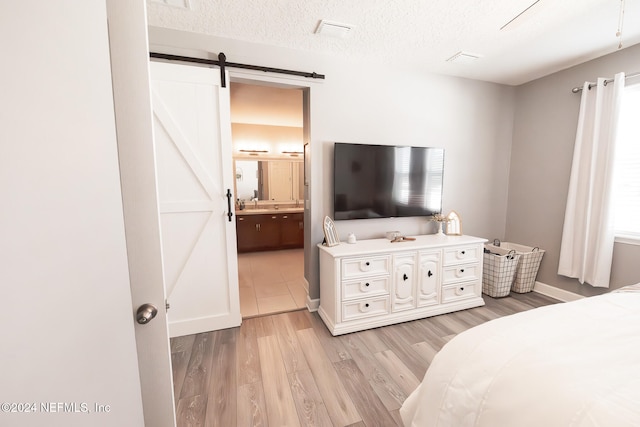 bedroom with a textured ceiling, a barn door, ensuite bathroom, and light hardwood / wood-style flooring