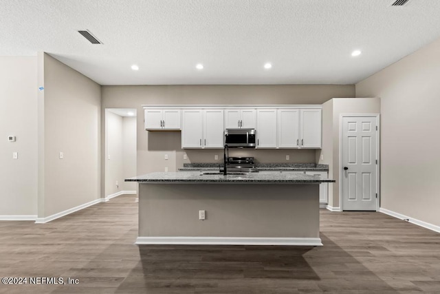 kitchen with sink, hardwood / wood-style floors, white cabinetry, dark stone counters, and a center island with sink