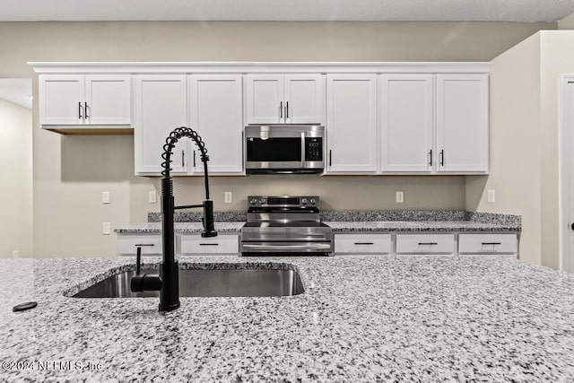 kitchen featuring sink, white cabinets, light stone counters, and stainless steel appliances