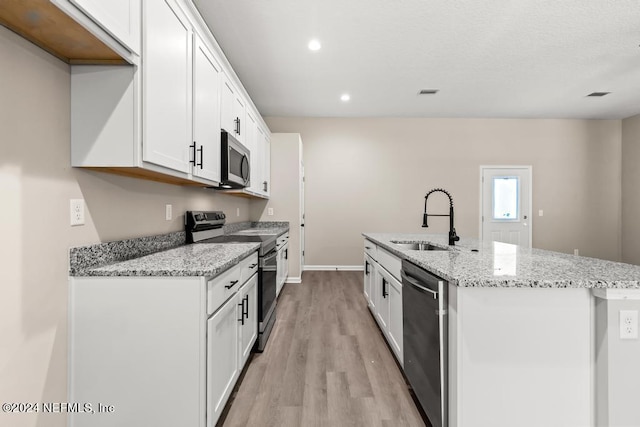 kitchen with a kitchen island with sink, light hardwood / wood-style flooring, stainless steel appliances, sink, and white cabinetry