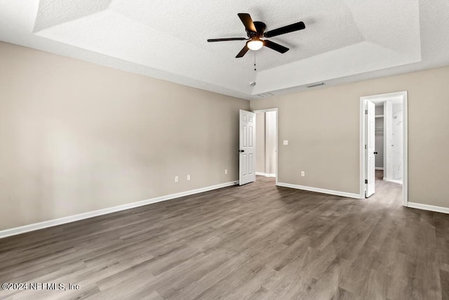 unfurnished bedroom with a walk in closet, a textured ceiling, a tray ceiling, ceiling fan, and dark hardwood / wood-style floors