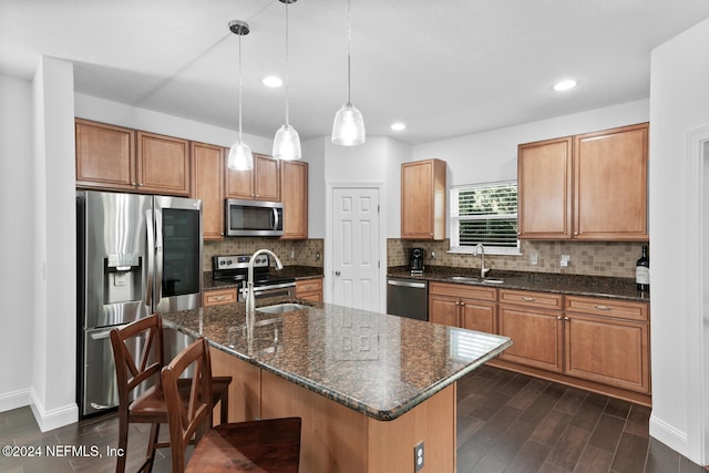 kitchen featuring stainless steel appliances, a kitchen island with sink, a sink, and pendant lighting