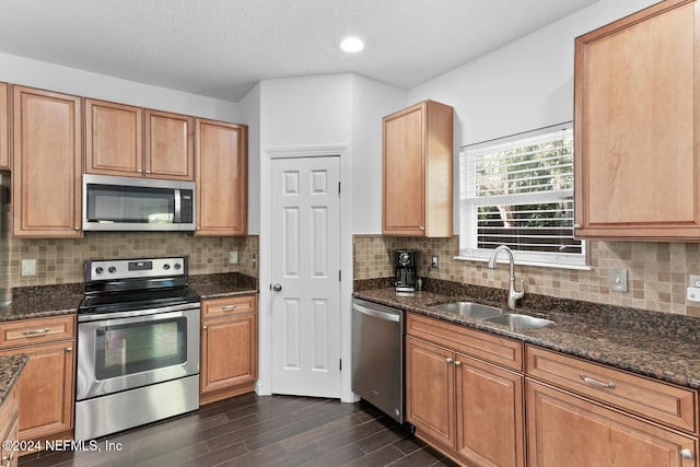 kitchen with tasteful backsplash, appliances with stainless steel finishes, a sink, dark wood finished floors, and dark stone counters