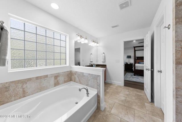 ensuite bathroom with ensuite bathroom, vanity, visible vents, a bath, and a textured ceiling