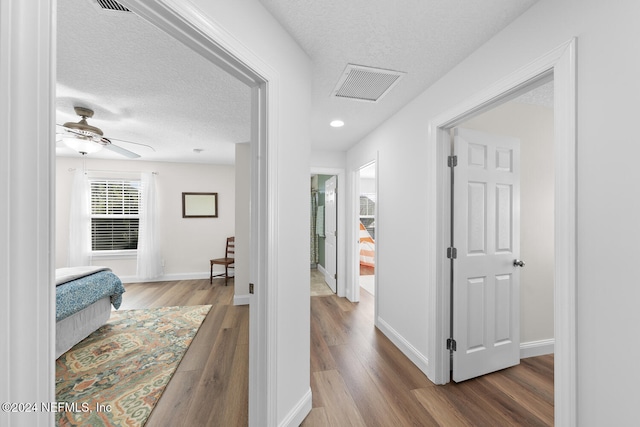 corridor with a textured ceiling, visible vents, and wood finished floors