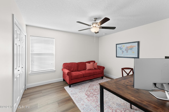 home office with baseboards, ceiling fan, light wood-style floors, and a textured ceiling