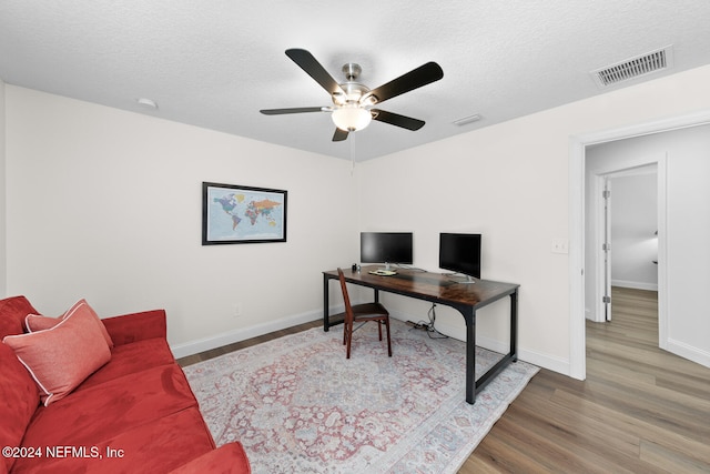 office featuring ceiling fan, visible vents, wood finished floors, and a textured ceiling