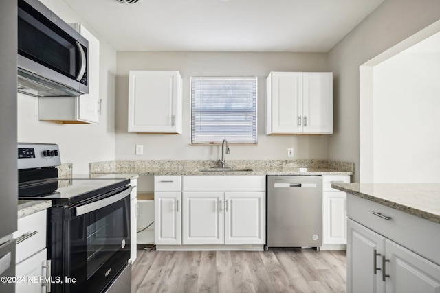 kitchen with stainless steel appliances, light hardwood / wood-style floors, white cabinetry, sink, and light stone counters