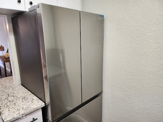 interior details with stainless steel fridge, white cabinets, and light stone counters