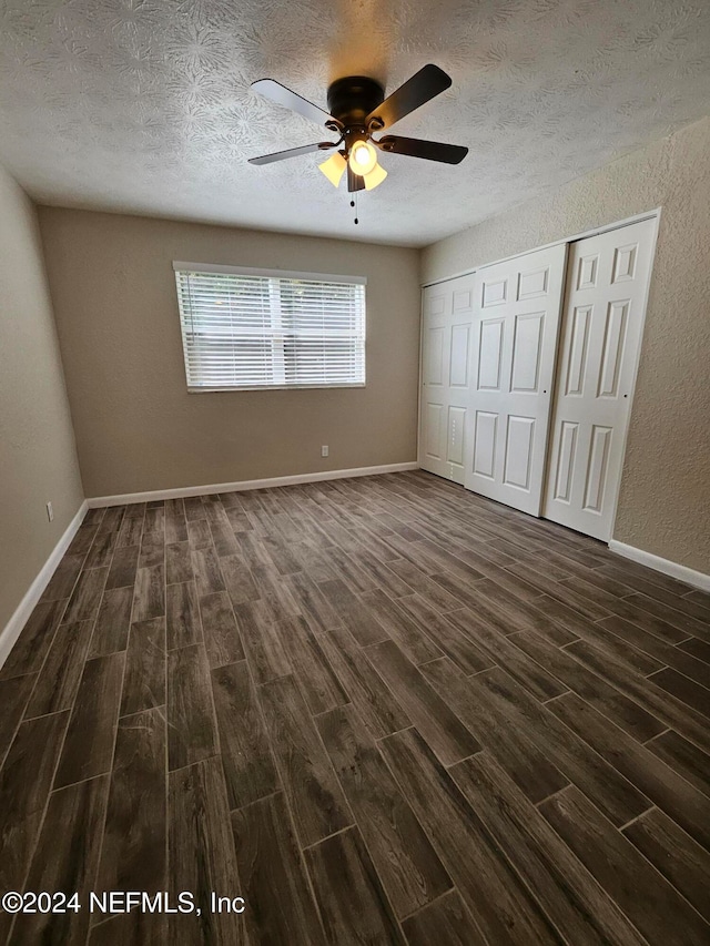 unfurnished bedroom with ceiling fan, a textured ceiling, a closet, and dark hardwood / wood-style flooring